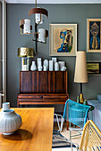 Secretary desk with collection of vases resting on top of it, above artwork on grey wall