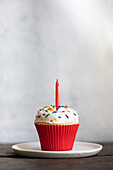 Buttercreme-Cupcake mit Zuckerstreusel und einer Kerze