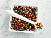 Bowl with mixed peppercorns and spoon with crushed peppercorns