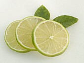 Three lime slices with leaves on a light background
