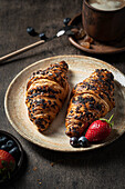 Croissants on a plate with a cup of coffee and fresh berries on a wooden table
