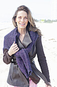 Long-haired woman in a dark coat with a sweater over her shoulders on the beach