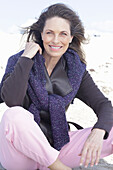 Long-haired woman in a dark coat with a sweater over her shoulders on the beach