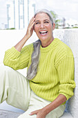 A laughing grey-haired woman wearing a greenish-yellow knitted sweater and light-coloured trousers