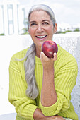 Grauhaarige Frau mit einem Apfel in grüngelbem Strickpullover