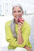 Grauhaarige Frau mit einem Apfel in grüngelbem Strickpullover