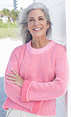 Grauhaarige Frau in pinkfarbenem Pullover am Strand