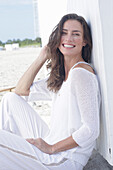 Happy, long-haired woman in white jumper and white trousers on the beach