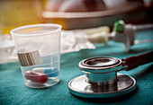 Stethoscope next to pills in a plastic cup, conceptual image