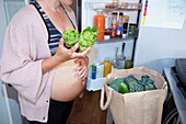 Pregnant woman putting away healthy groceries in kitchen