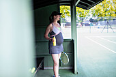 Pregnant woman in dress drinking water at tennis court