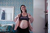 Happy pregnant woman putting on sweater near wardrobe