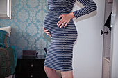 Pregnant woman in dress holding baby bump at bedroom closet