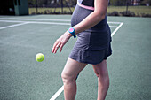 Pregnant woman bouncing tennis ball on tennis court