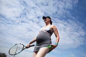 Pregnant woman in dress playing tennis below sunny sky