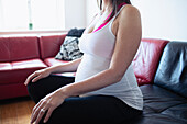 Pregnant woman in tank top meditating on living room sofa