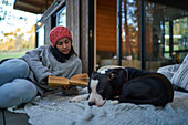 Woman reading book next to dog on cabin patio