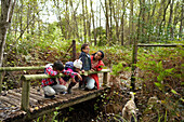 Mother and children with dog on footbridge in woods