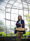 Smiling young woman gardening below trellis