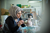 Female artist in hijab painting ceramics in art studio