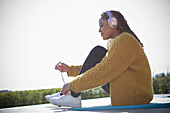 Young woman with headphones tying shoelace outdoors