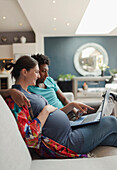 Pregnant couple with laptop on living room sofa