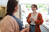 Young women friends talking and drinking coffee in kitchen