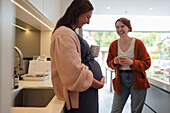 Happy pregnant woman with friend in kitchen
