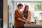 Happy female friends cutting loaf cake in kitchen