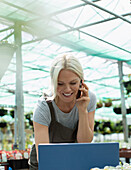 Smiling female garden shop owner talking on smart phone