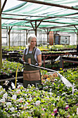 Female garden shop owner watering plants with hose