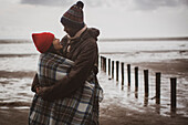 Happy couple wrapped in blanket on winter beach