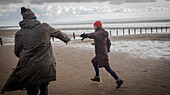 Couple in warm clothing running on winter ocean beach