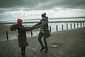 Happy playful couple holding hands on winter beach