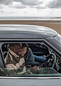 Happy couple using smart phone inside car on winter beach