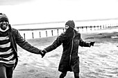 Couple in warm clothing holding hands on winter beach
