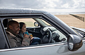 Happy couple drinking tea in car on wet winter beach