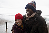 Happy couple in warm clothing hugging on winter beach