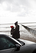 Couple in warm clothing hugging on wet winter beach