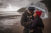 Happy couple under umbrella on wet winter beach
