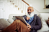 Bearded man using digital tablet on living room sofa