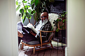 Mature man with beard reading book in armchair at home