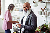 Happy mature man with beard drinking coffee in kitchen