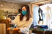 Female shop owner in face mask arranging display in boutique