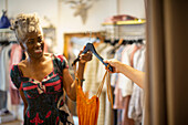 Female shop owner handing dress on hanger to customer