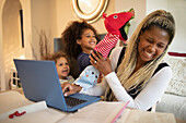 Daughters with puppets distracting mother working at laptop