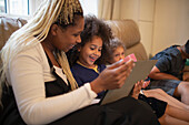 Happy mother and daughter using tablet on living room sofa