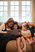 Mother and daughters using tablet on living room sofa