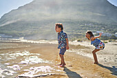 Brother and sister playing in sunny ocean surf on beach