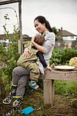 Happy mother holding tired toddler son on allotment